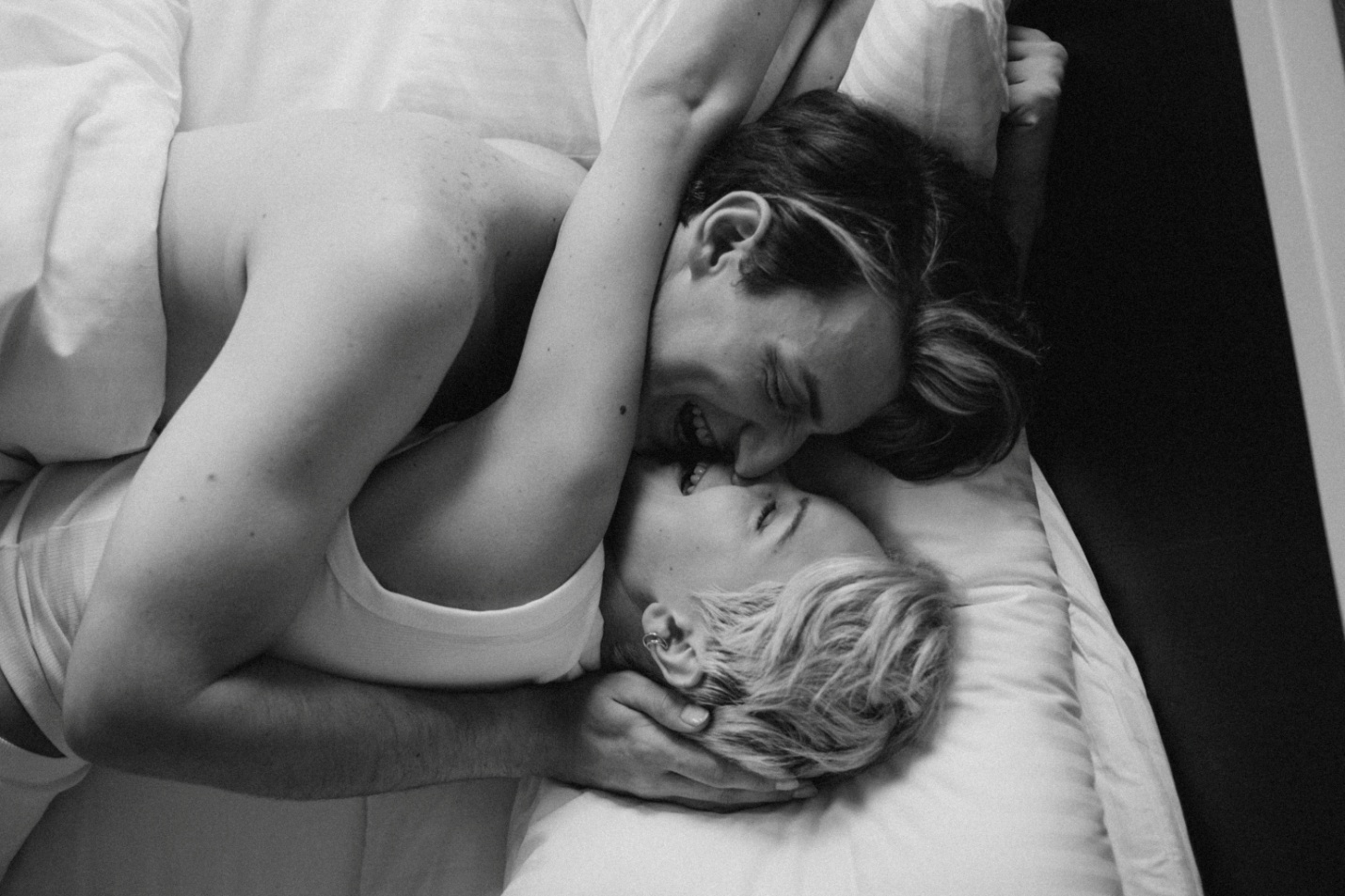 A b&w photo of a couple lying in bed and laughing