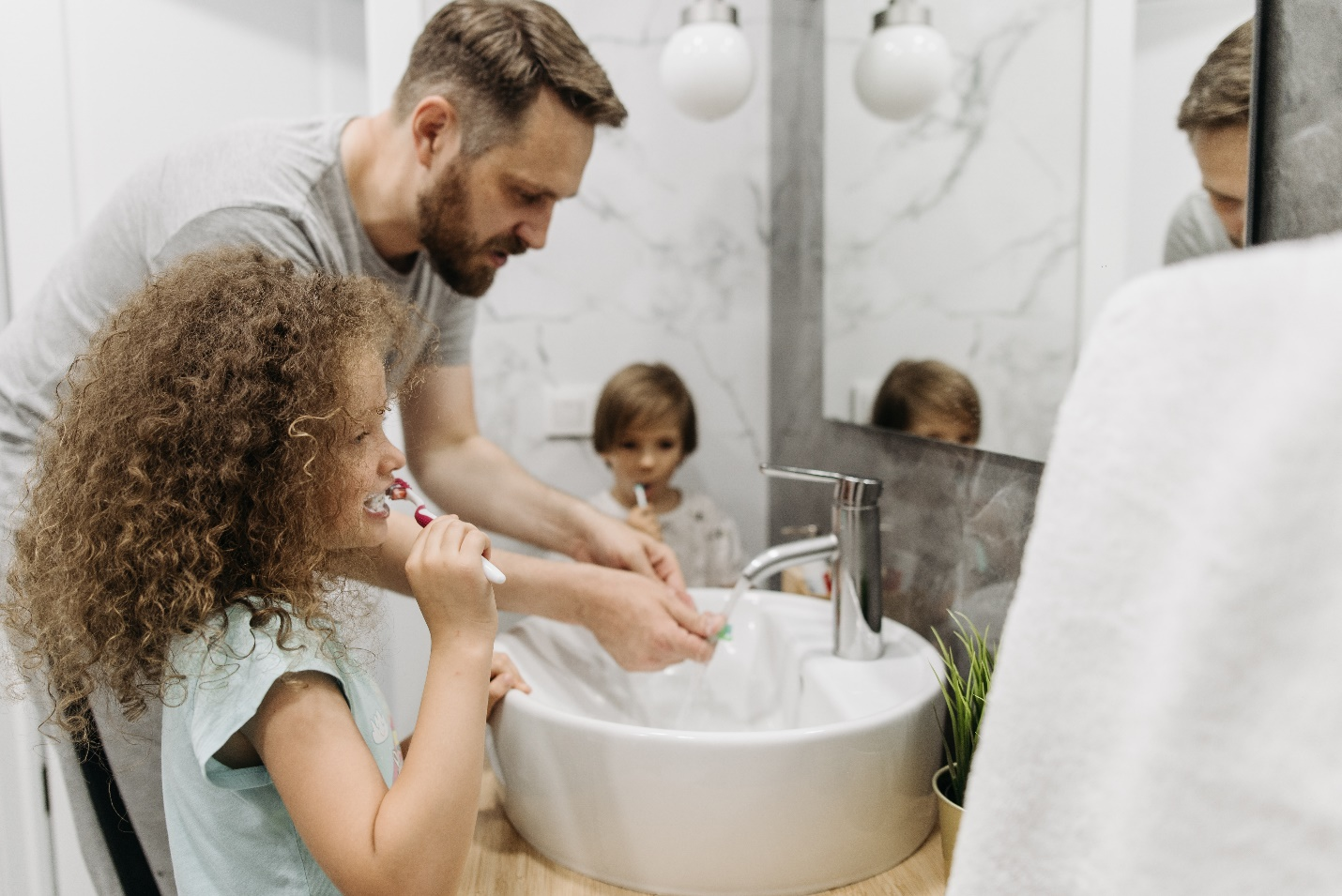 A man cleans his brush while children brush their teeth