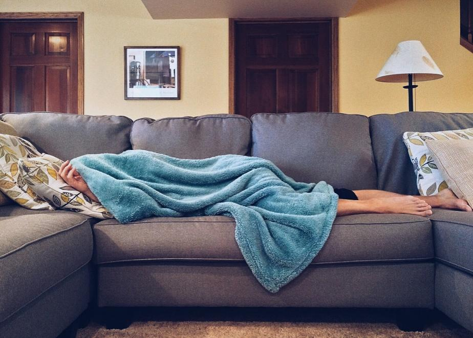 A person lying on a sofa covered in a fluffy blue blanket