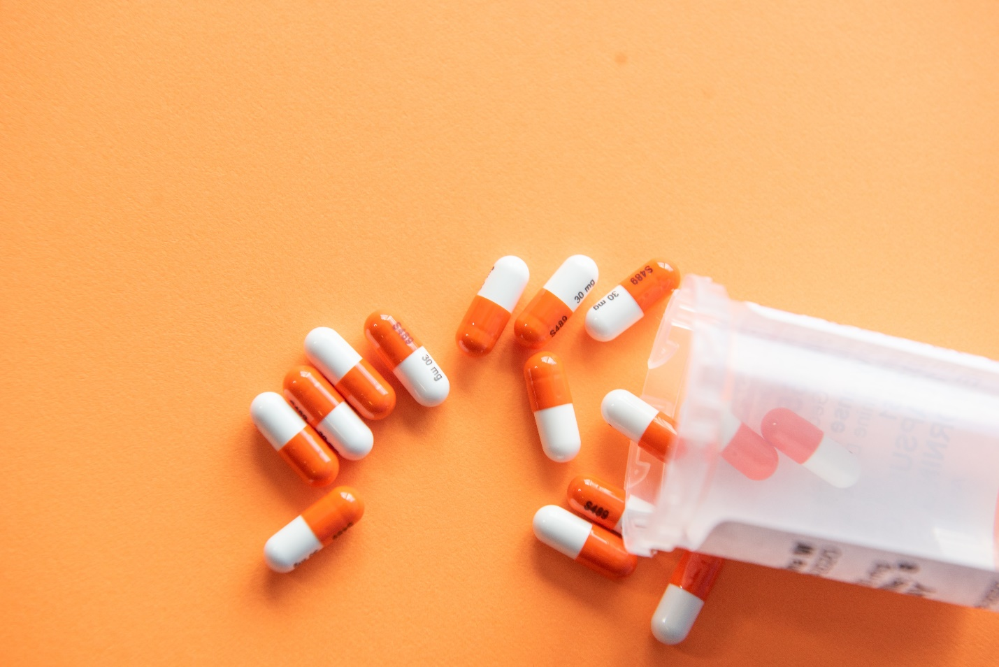 White and orange pills scattered against a peach background