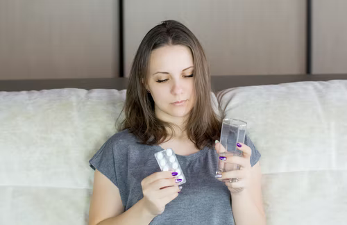 A woman holding a glass of water and a tablet strip