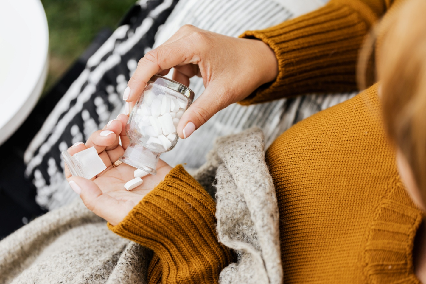 Woman wearing a mustard sweater dropping pills into her hand from a pill bottle